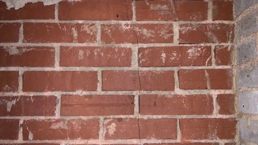 HydroHelp911 Crawl Space & Foundation Repair inspecting a thin vertical crack in a red brick foundation wall