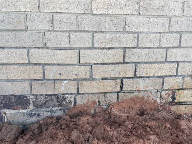 HydroHelp911 Crawl Space & Foundation Repair inspecting a stair step crack in a tan brick foundation wall.
