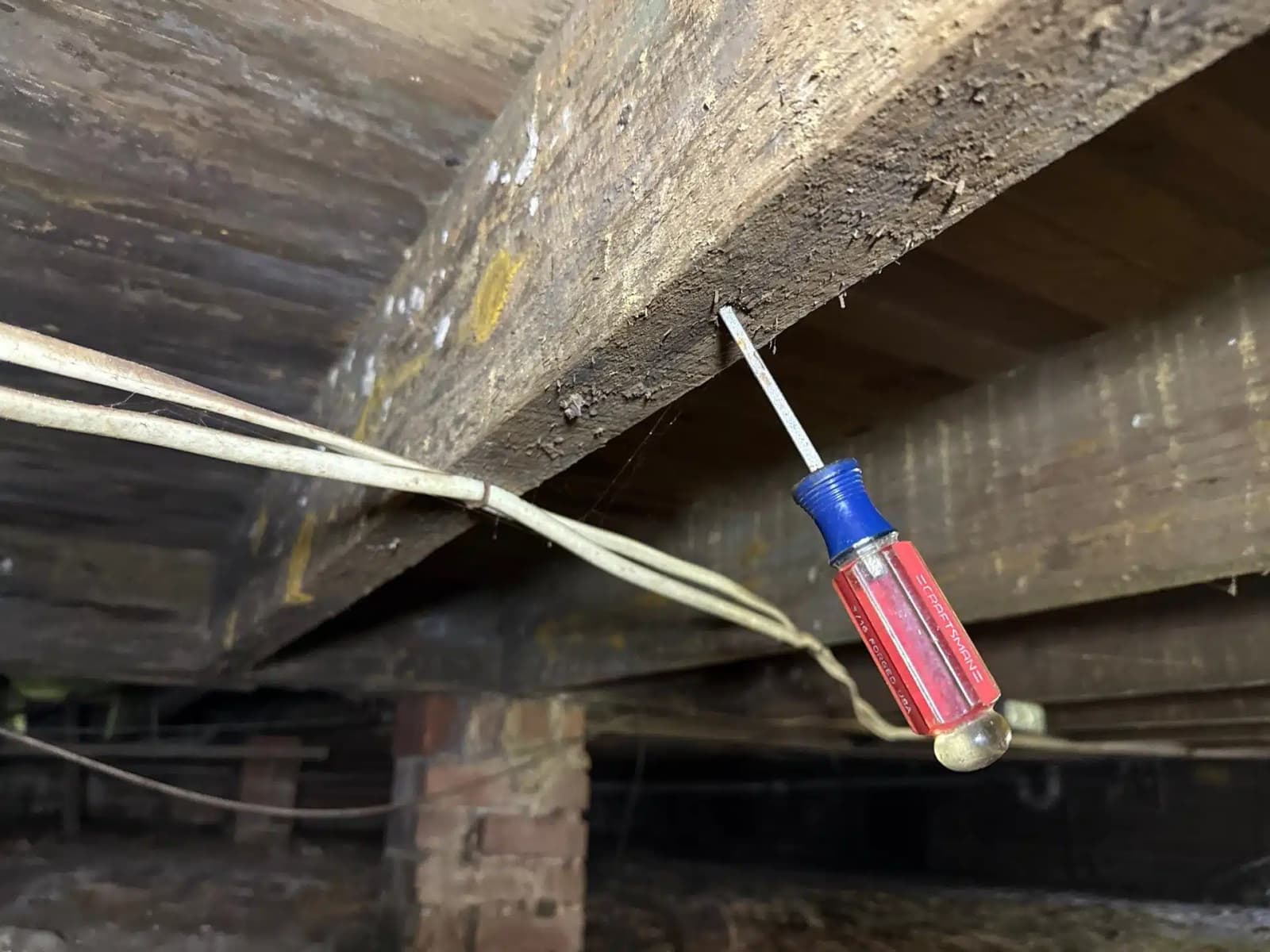 HydroHelp911 Crawl Space & Foundation Repair inspecting a rotted floor joist for dry rot damage in a crawl space.