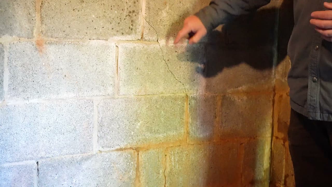 HydroHelp911 Crawl Space & Foundation Repair inspecting diagonal cracks and moisture on a basement block wall.
