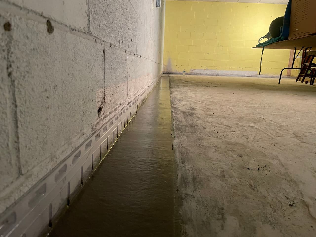 HydroHelp911 Crawl Space & Foundation Repair installing an interior drainage system in a basement with pooled water.