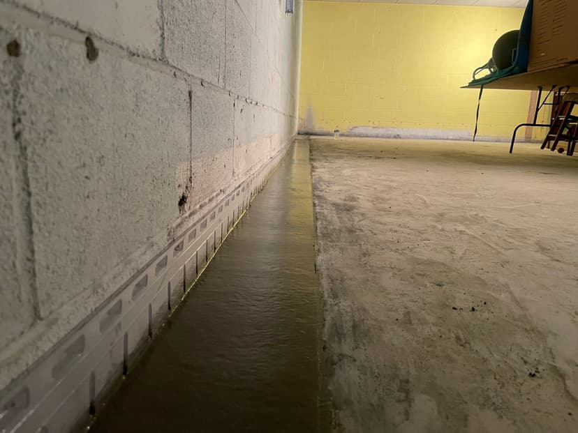HydroHelp911 Crawl Space & Foundation Repair installing an interior drainage system in a basement with pooled water.