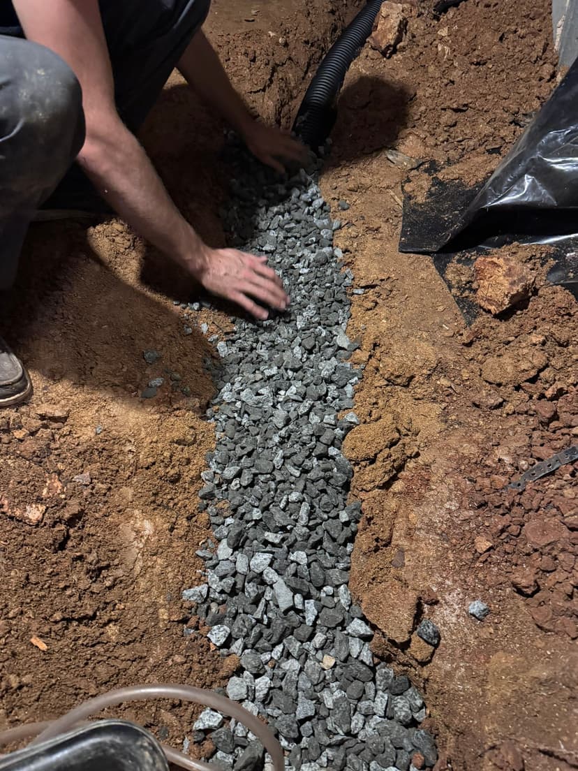 HydroHelp911 Crawl Space & Foundation Repair installing a crawl space drainage system with gravel and perforated pipe.