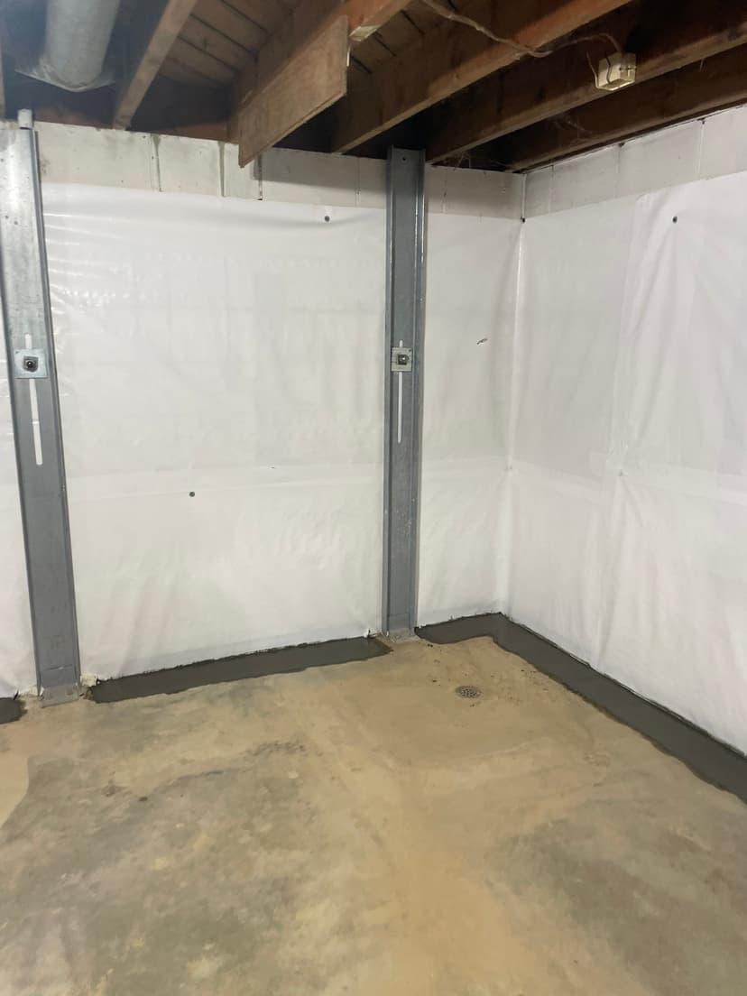 HydroHelp911 Crawl Space & Foundation Repair installing I-beam wall bracing and a vapor barrier in a basement.