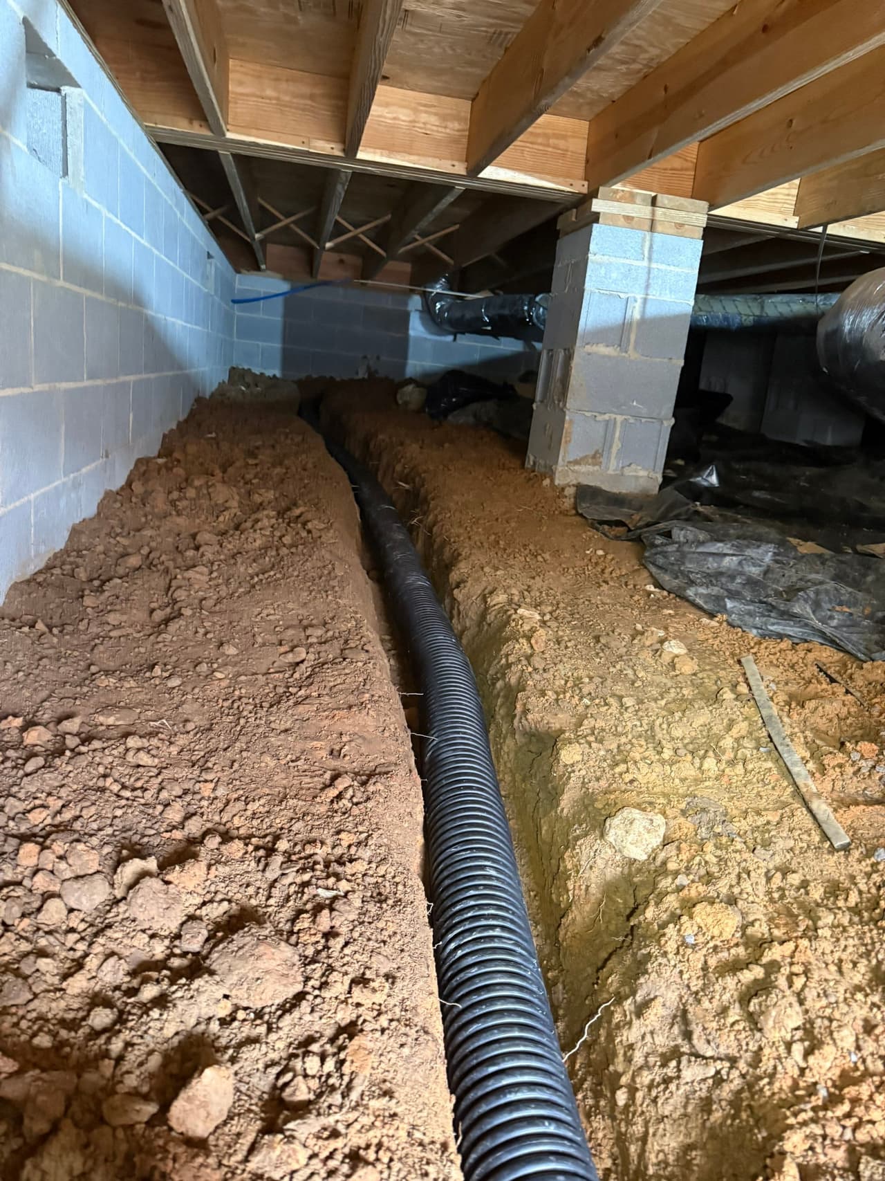 HydroHelp911 Crawl Space & Foundation Repair installing a perforated drainage pipe in a crawl space trench.