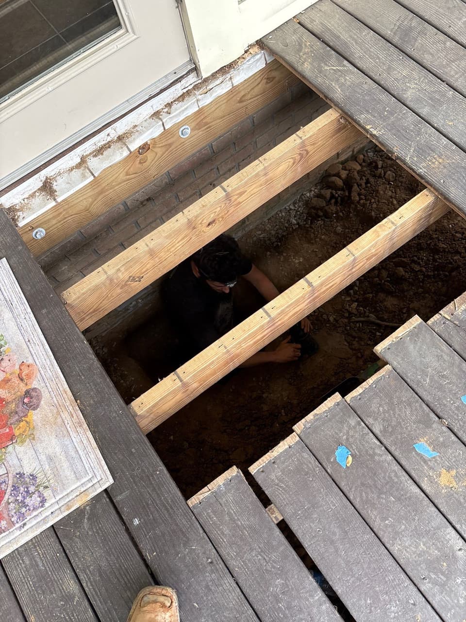 HydroHelp911 Crawl Space & Foundation Repair team member working in an excavation under a deck in Greensboro.