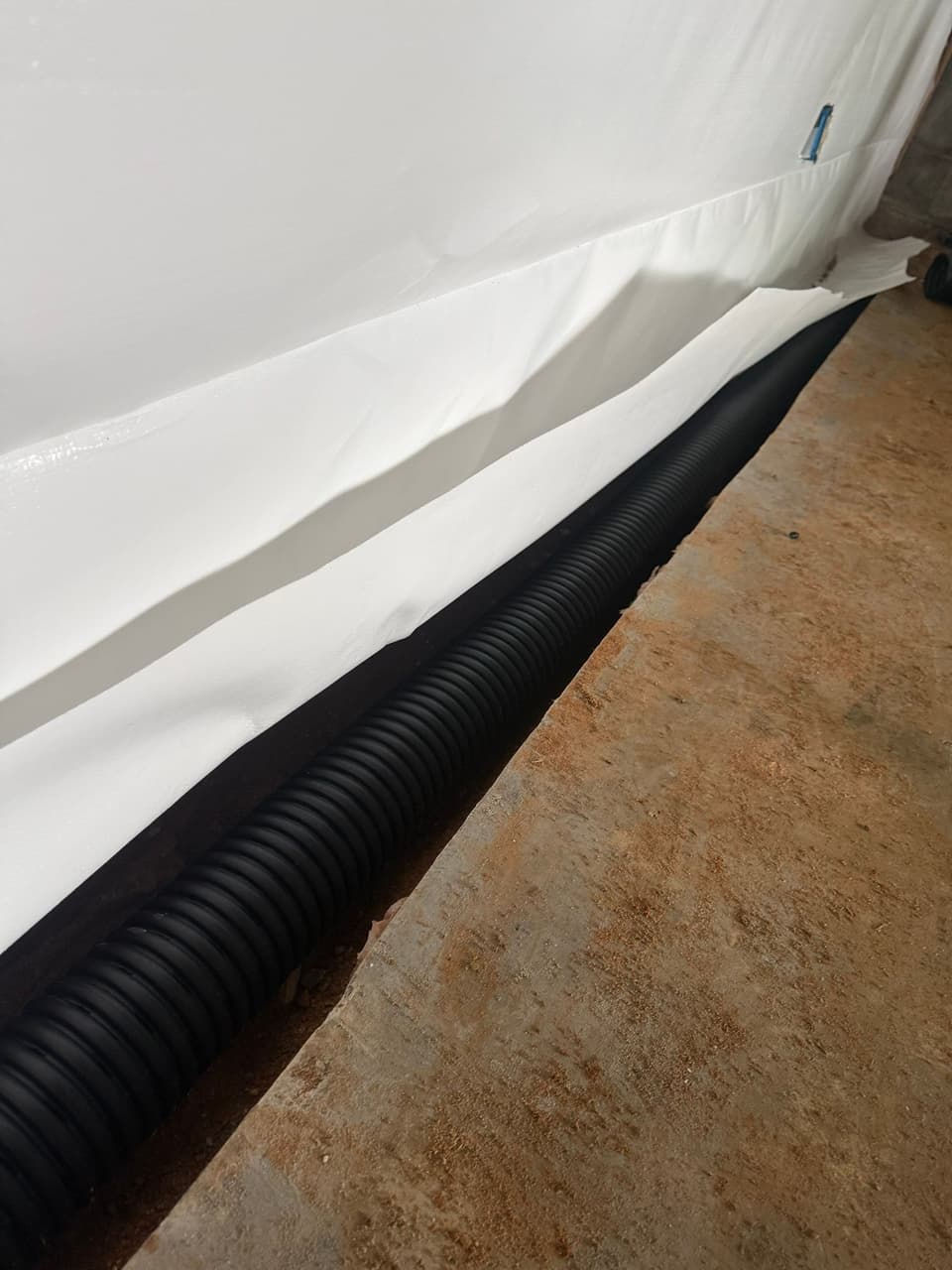 HydroHelp911 Crawl Space & Foundation Repair installing a basement interior drainage system with a vapor barrier.