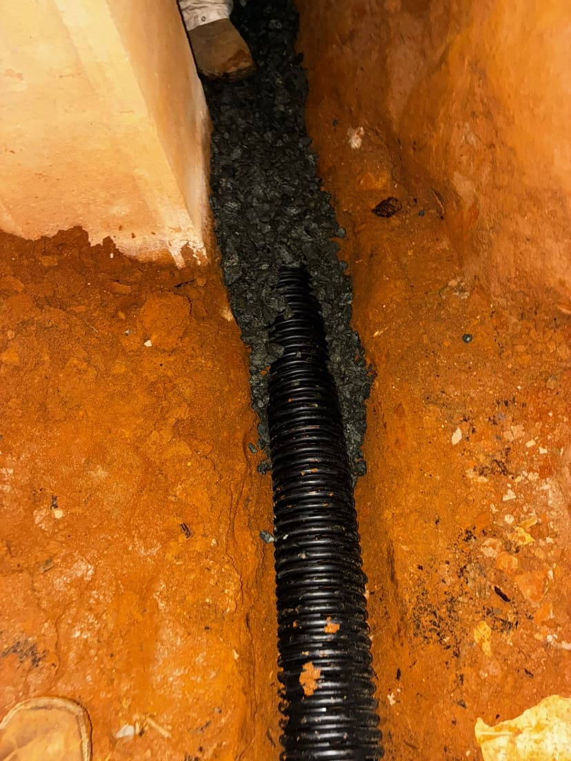 HydroHelp911 Crawl Space & Foundation Repair installing a perforated drainage pipe in a crawl space trench.