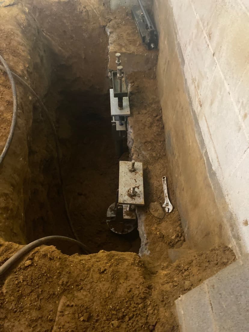HydroHelp911 Crawl Space & Foundation Repair installing steel piers with a hydraulic ram and footing bracket.