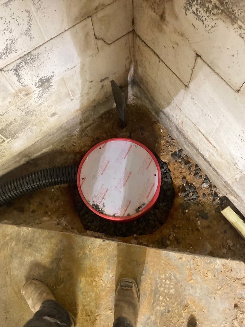 HydroHelp911 Crawl Space & Foundation Repair installing an interior drainage system and sump pit in a basement corner.
