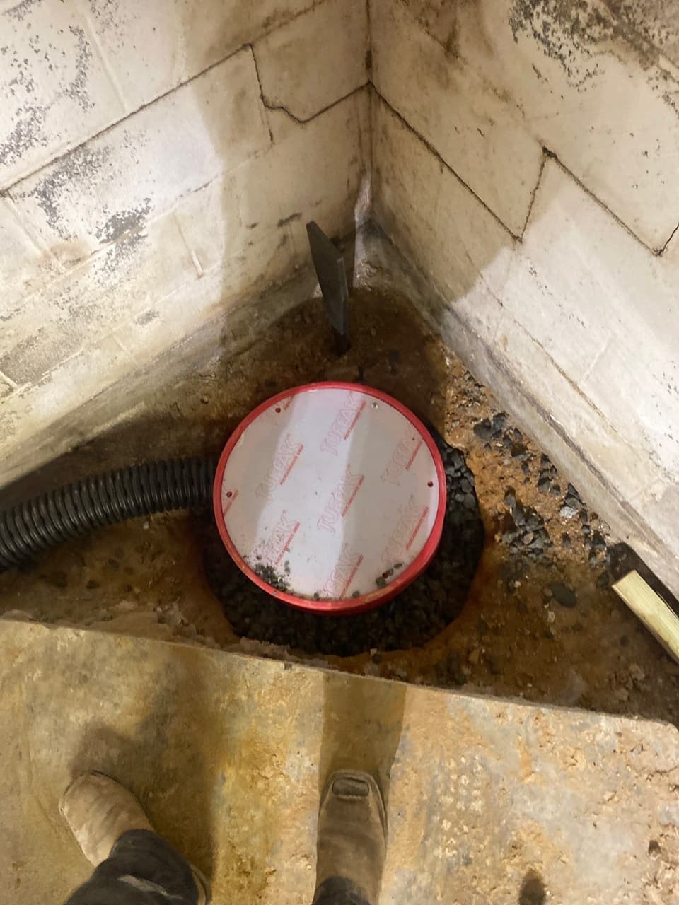 HydroHelp911 Crawl Space & Foundation Repair installing an interior drainage system and sump pit in a basement corner.