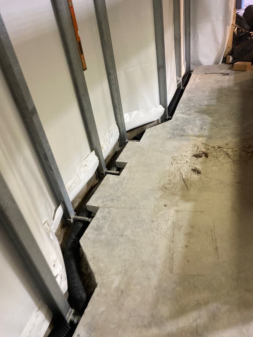 HydroHelp911 Crawl Space & Foundation Repair installing an interior drainage system with drainage pipe in a basement.