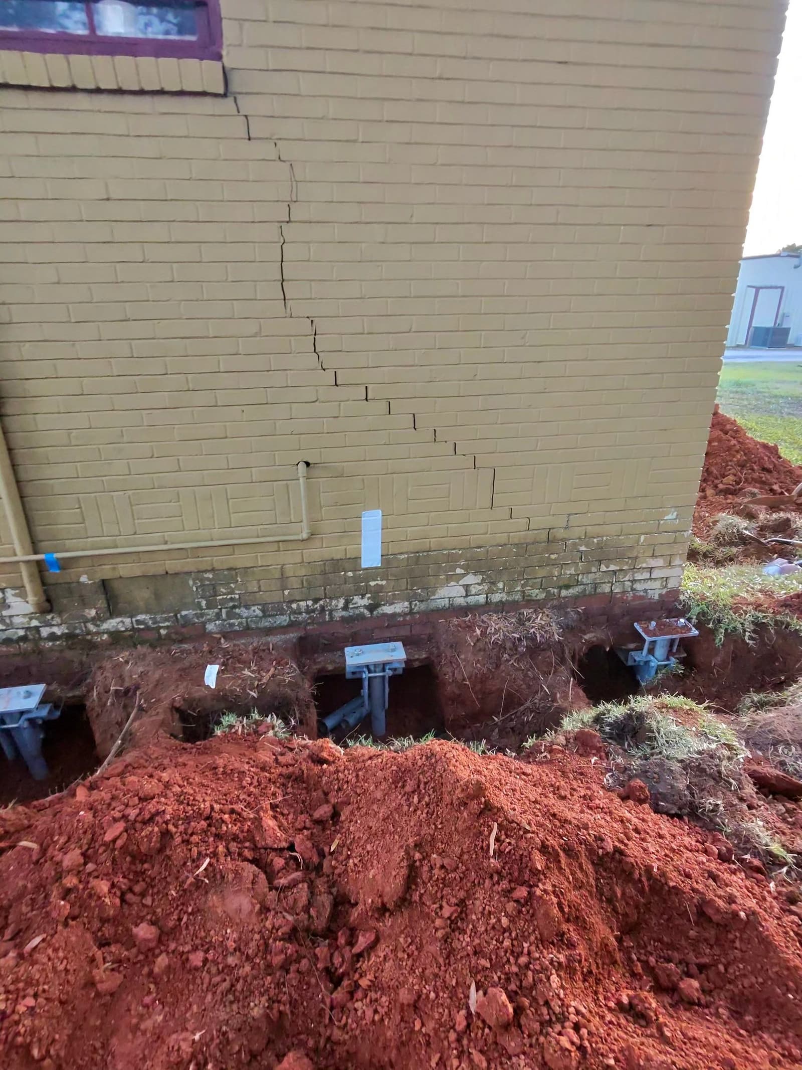 HydroHelp911 Crawl Space & Foundation Repair installing steel piers for foundation underpinning on a brick foundation
