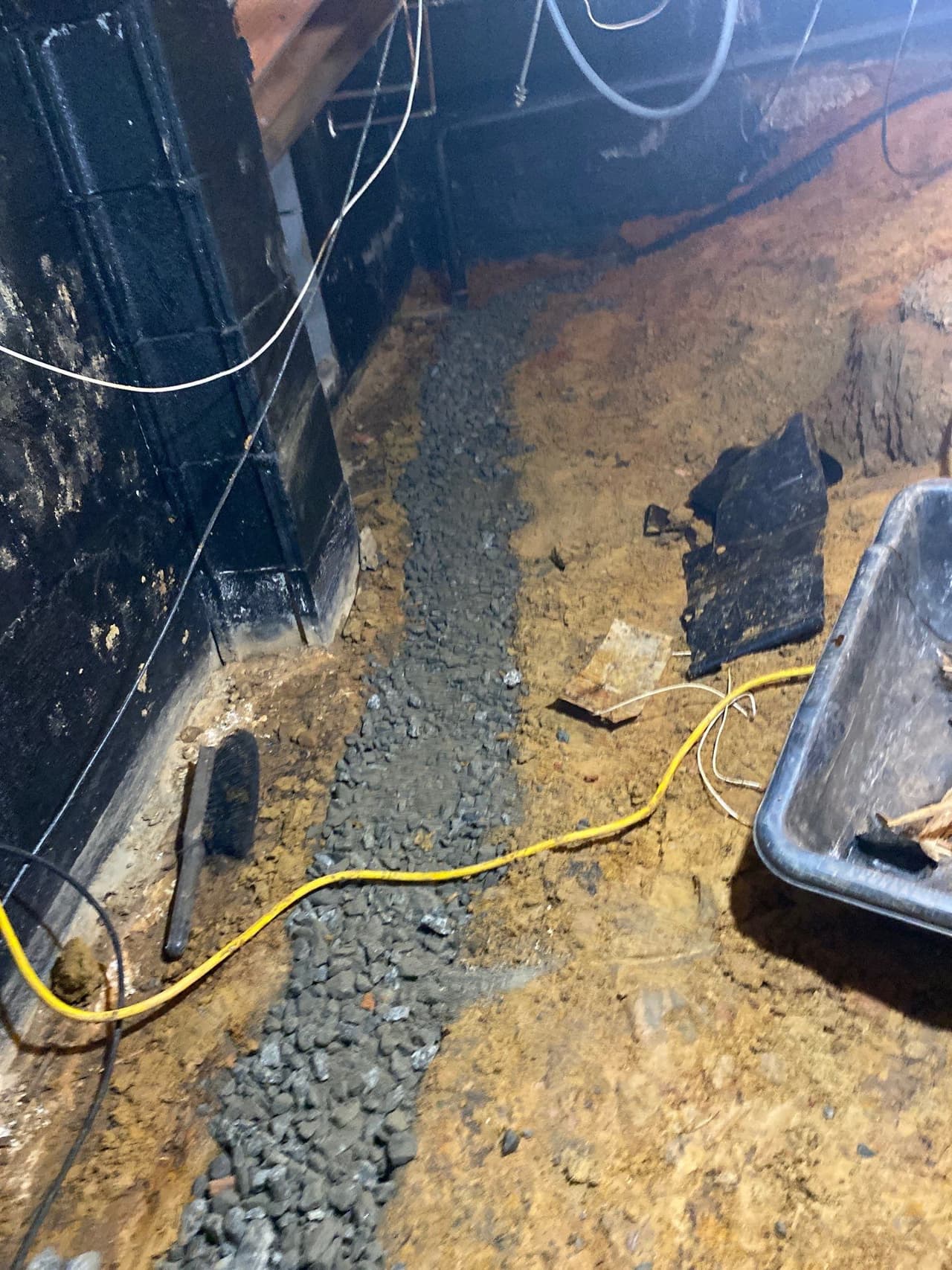HydroHelp911 Crawl Space & Foundation Repair installing a crawl space drainage system with gravel in a trench.