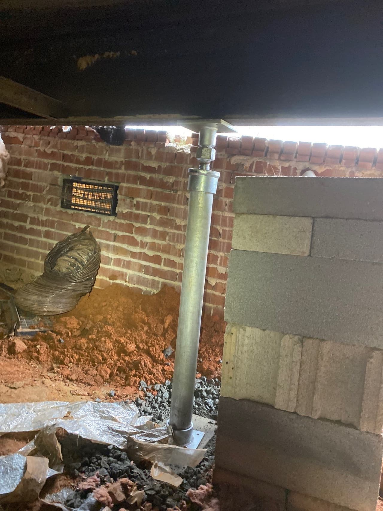 HydroHelp911 Crawl Space & Foundation Repair installing a crawl space jack under a brick foundation, with a crawl space vent
