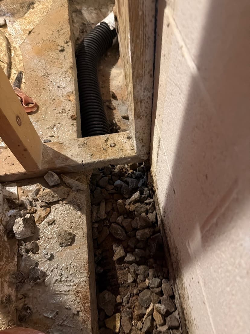HydroHelp911 Crawl Space & Foundation Repair installing a drainage system in a crawl space trench with perforated pipe.
