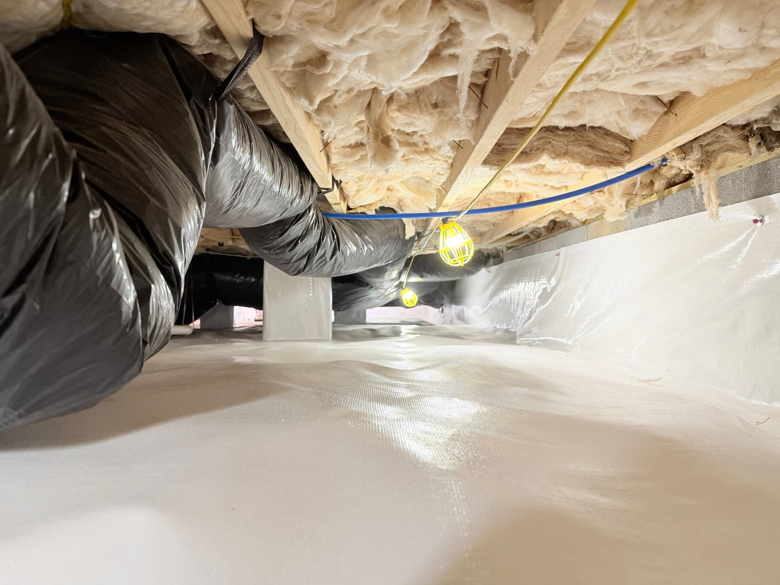 HydroHelp911 Crawl Space & Foundation Repair installing a white vapor barrier and insulation in a crawl space.