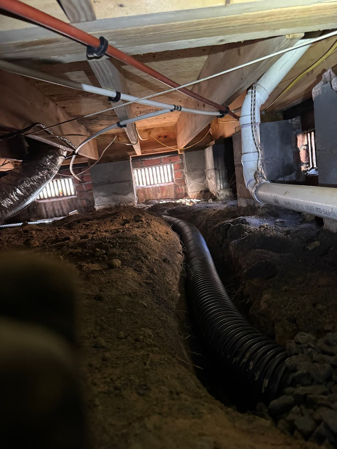 HydroHelp911 Crawl Space & Foundation Repair installing a perforated drainage pipe in a trench within a crawl space.