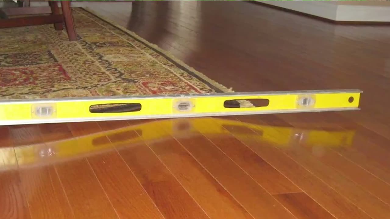 Inspecting an uneven hardwood floor with a spirit level, indicating the need