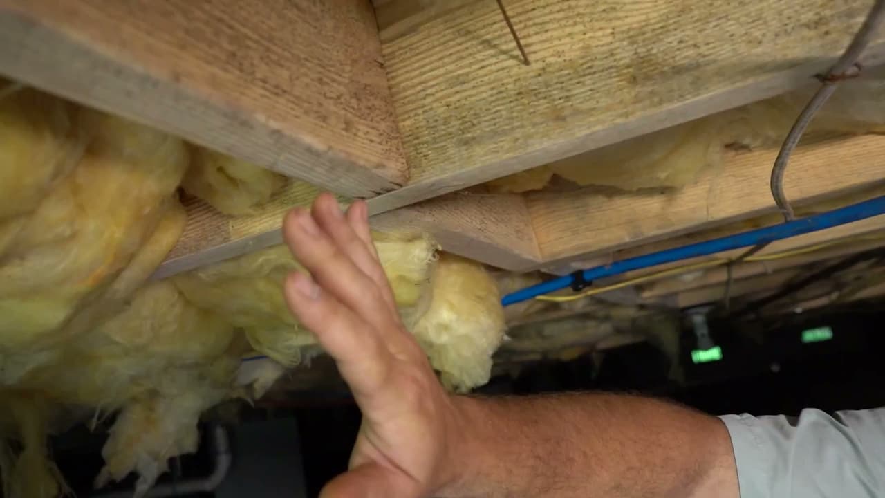 Technician inspecting deteriorating crawl space insulation and moisture damage.