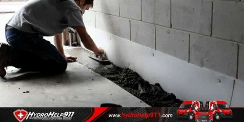 Worker setting an interior drainage channel along a basement wall