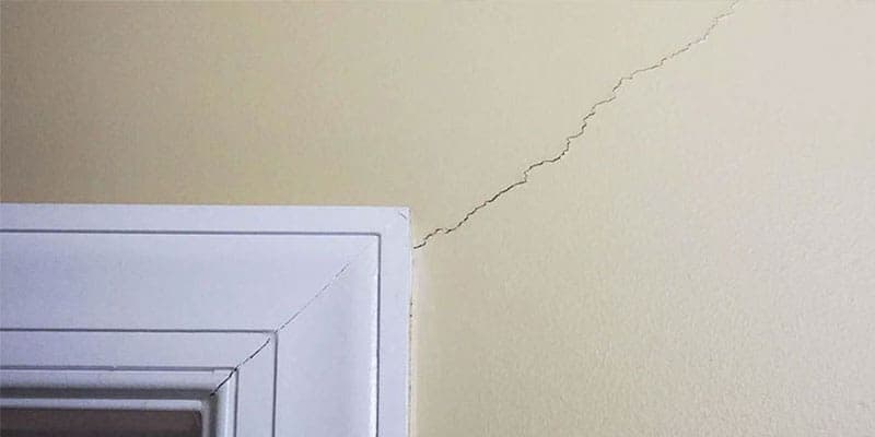 Hairline crack running from the corner of a window frame across a wall