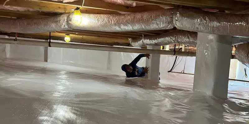 Technician working in an encapsulated crawl space under insulated ducts