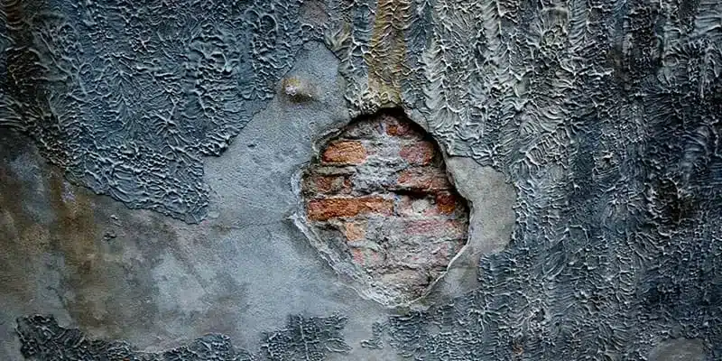 Damp, peeling wall surface with brick showing underneath