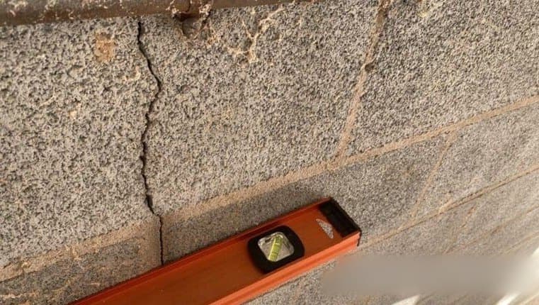 Vertical crack in a concrete block foundation wall with a level beside it