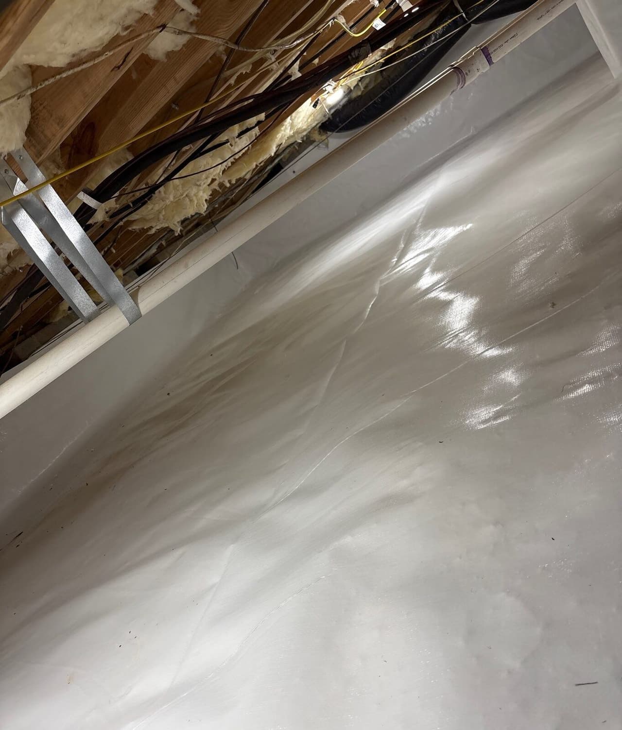 White liner covering the crawl space floor and wall below joists and a pipe.