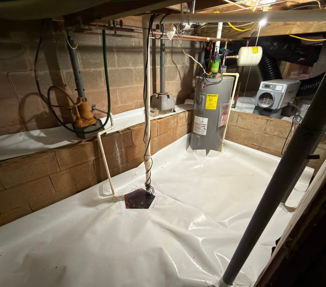Lined crawl space area with a sump pit, a dehumidifier on a ledge and a water heater standing on the liner.