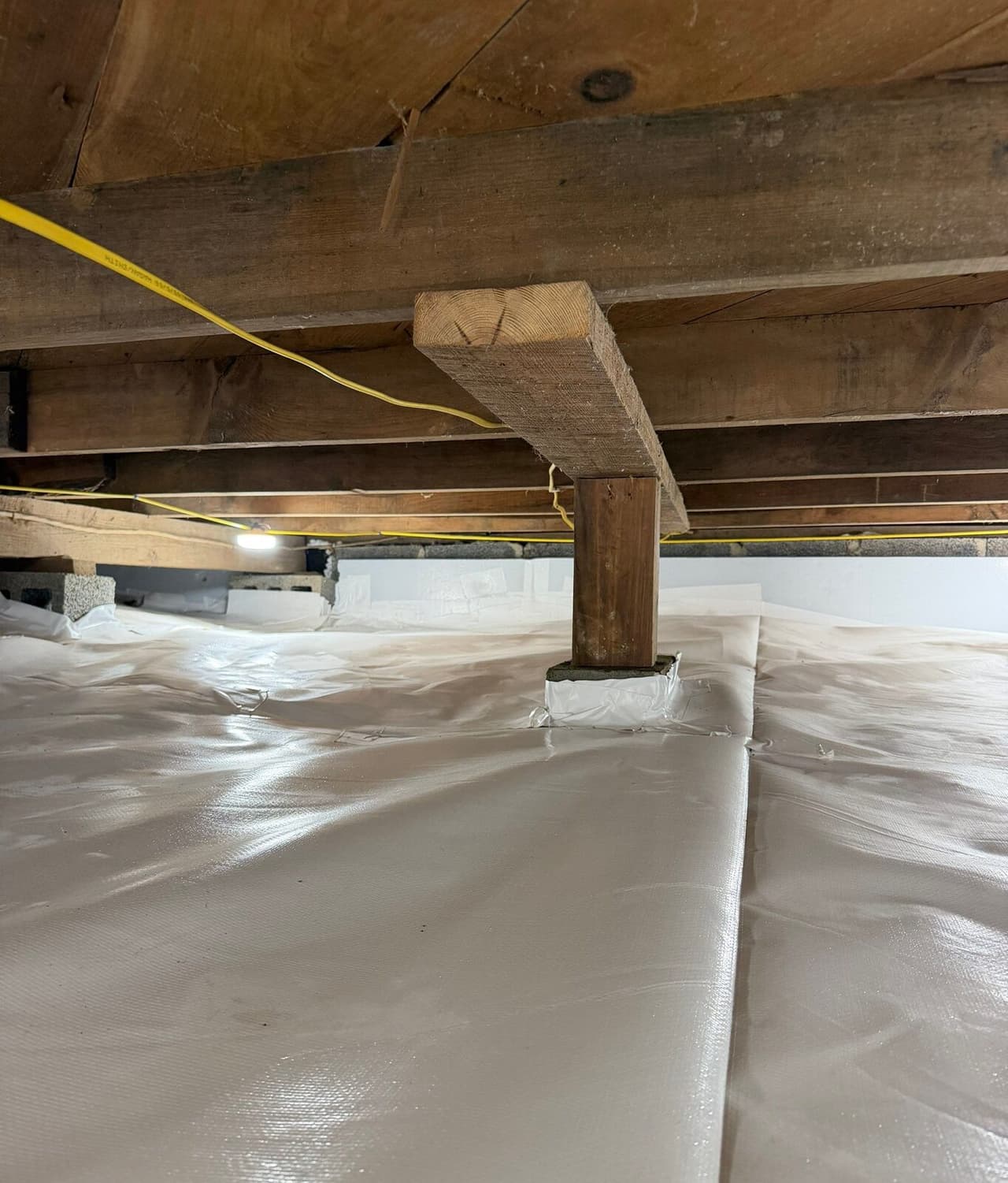 A wooden support post with its base wrapped in white liner in a fully lined crawl space.