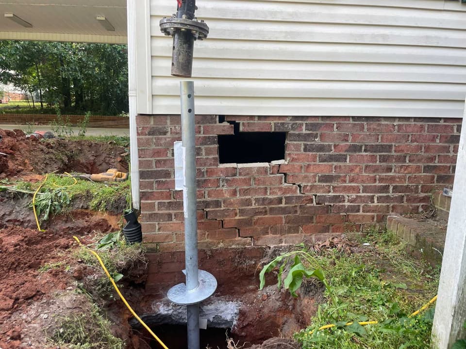 HydroHelp911 Crawl Space & Foundation Repair installing helical piers to repair a cracked brick foundation.
