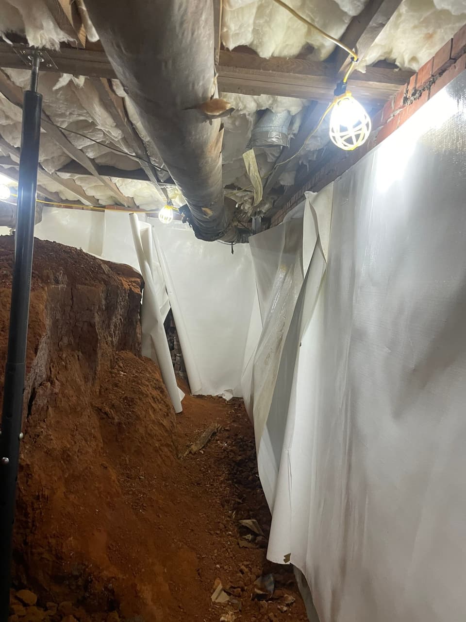 HydroHelp911 Crawl Space & Foundation Repair crew installing a vapor barrier and structural support jack in a crawl space.