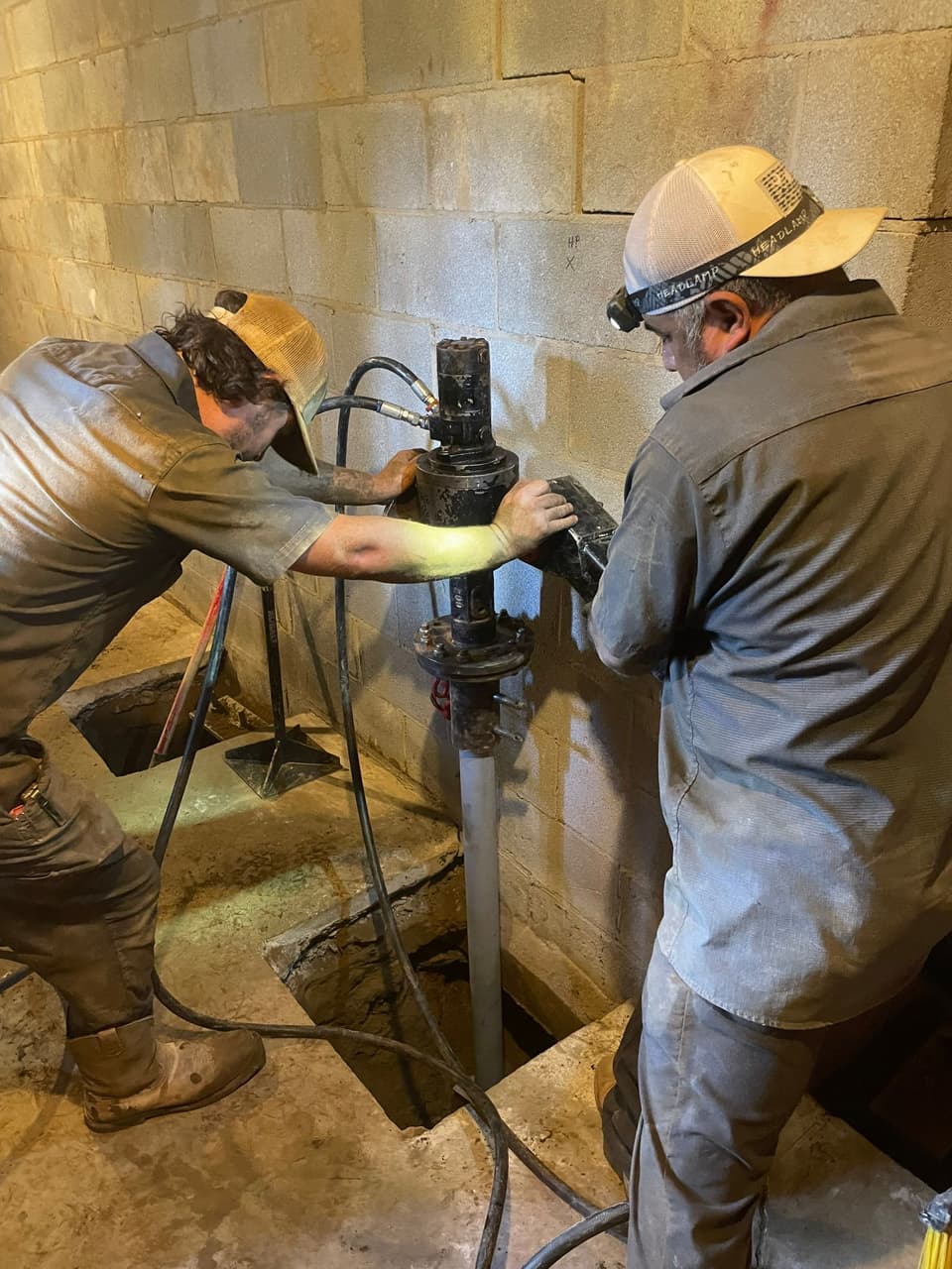 HydroHelp911 Crawl Space & Foundation Repair installing helical piers with a rotary drive head in a basement.