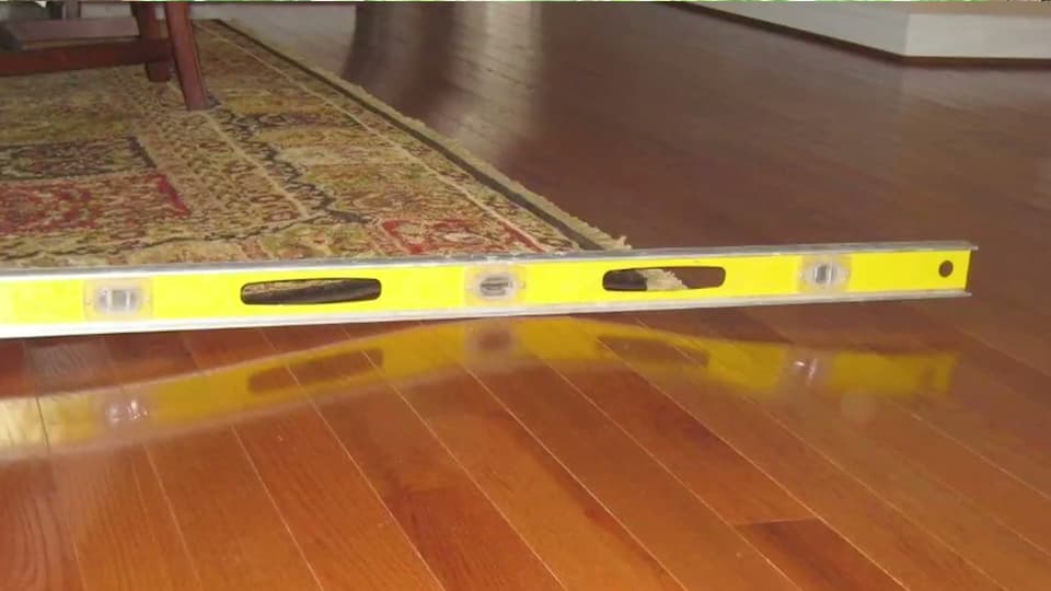 HydroHelp911 Crawl Space & Foundation Repair inspecting an uneven hardwood floor with a spirit level, indicating the need