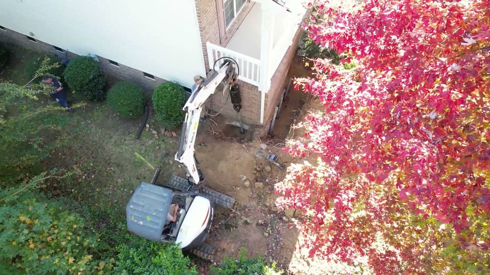 HydroHelp911 Crawl Space & Foundation Repair installing helical piers with a mini excavator and rotary drive head.