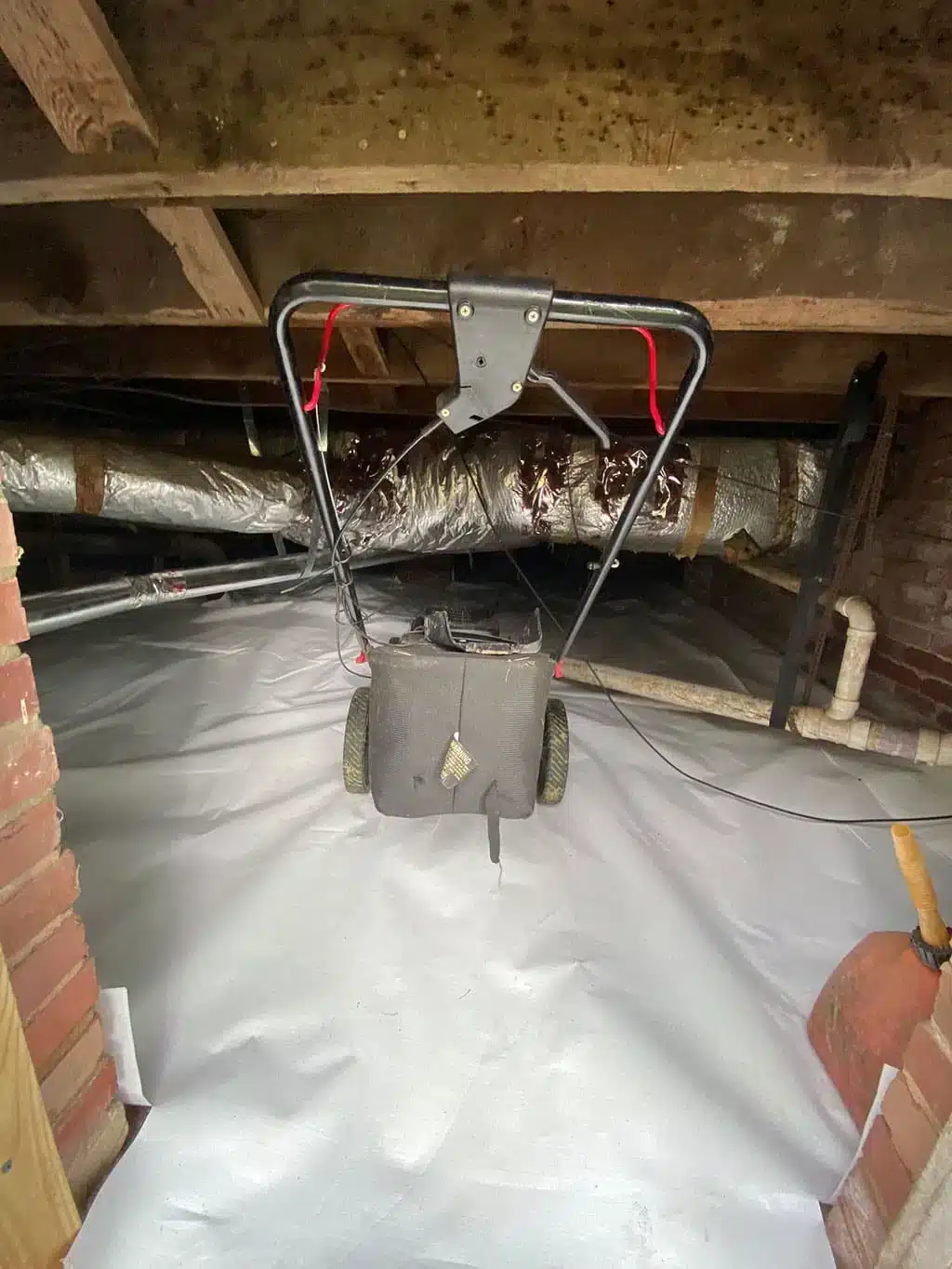 Crawl space with a white vapor barrier and a dehumidifier hung from the joists