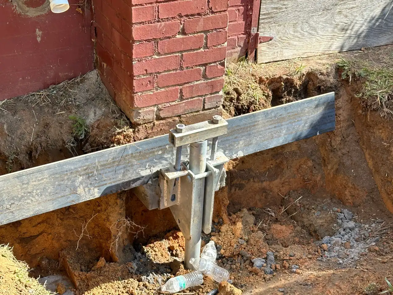 Steel pier bracket supporting a brick foundation in an excavated hole