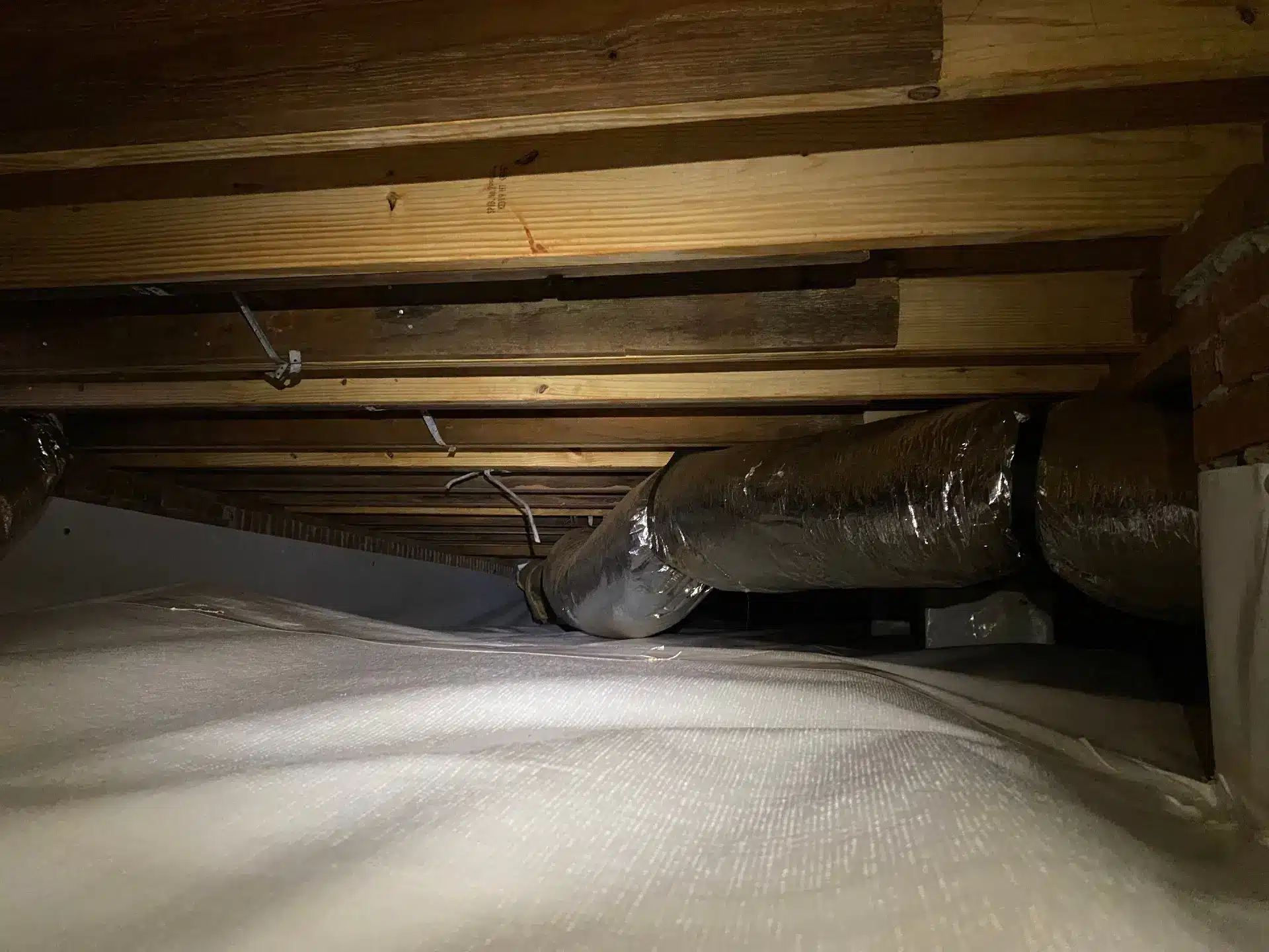 Extra lumber sistered alongside floor joists above a vapor barrier in a crawl space