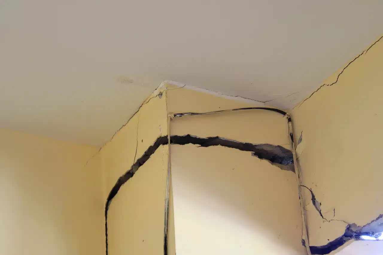 Severe horizontal structural cracks splitting a yellow interior wall near the ceiling.
