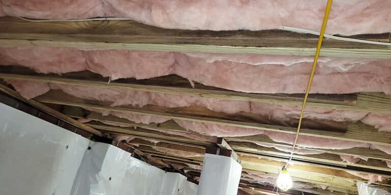 Pink fiberglass insulation between floor joists in a crawl space