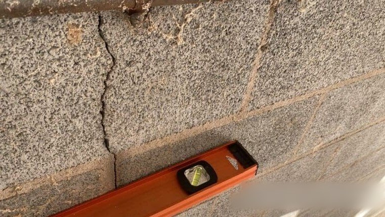 Vertical crack in a concrete block foundation wall with a level beside it