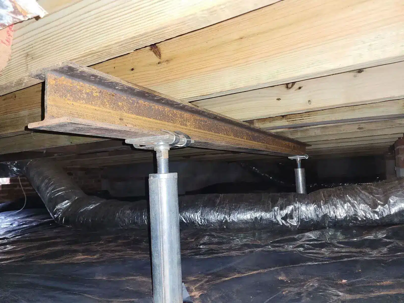Steel beam and adjustable jack posts supporting floor joists in a crawl space