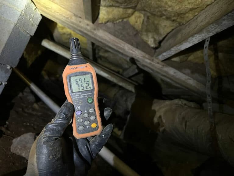 Gloved hand holding a humidity meter in a damp crawl space