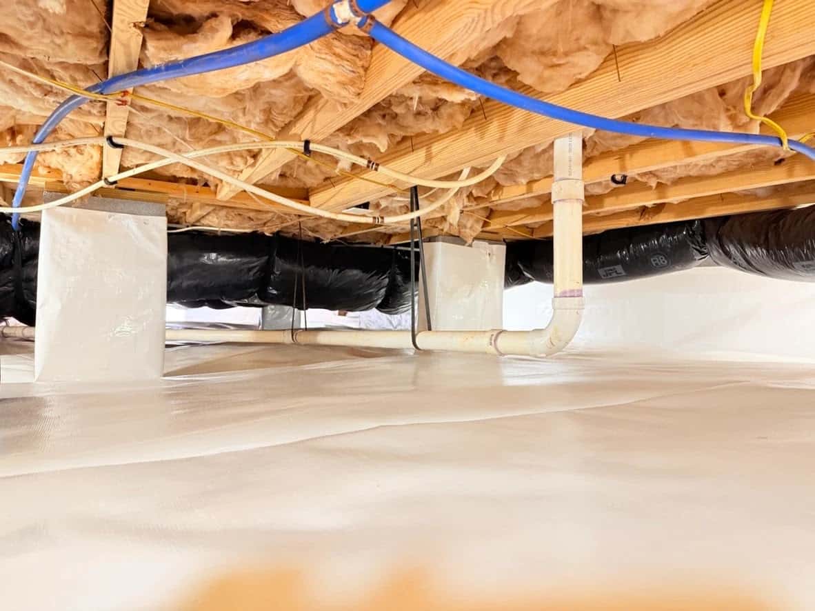 Crawl space with a white liner over the floor and piers under fiberglass insulation